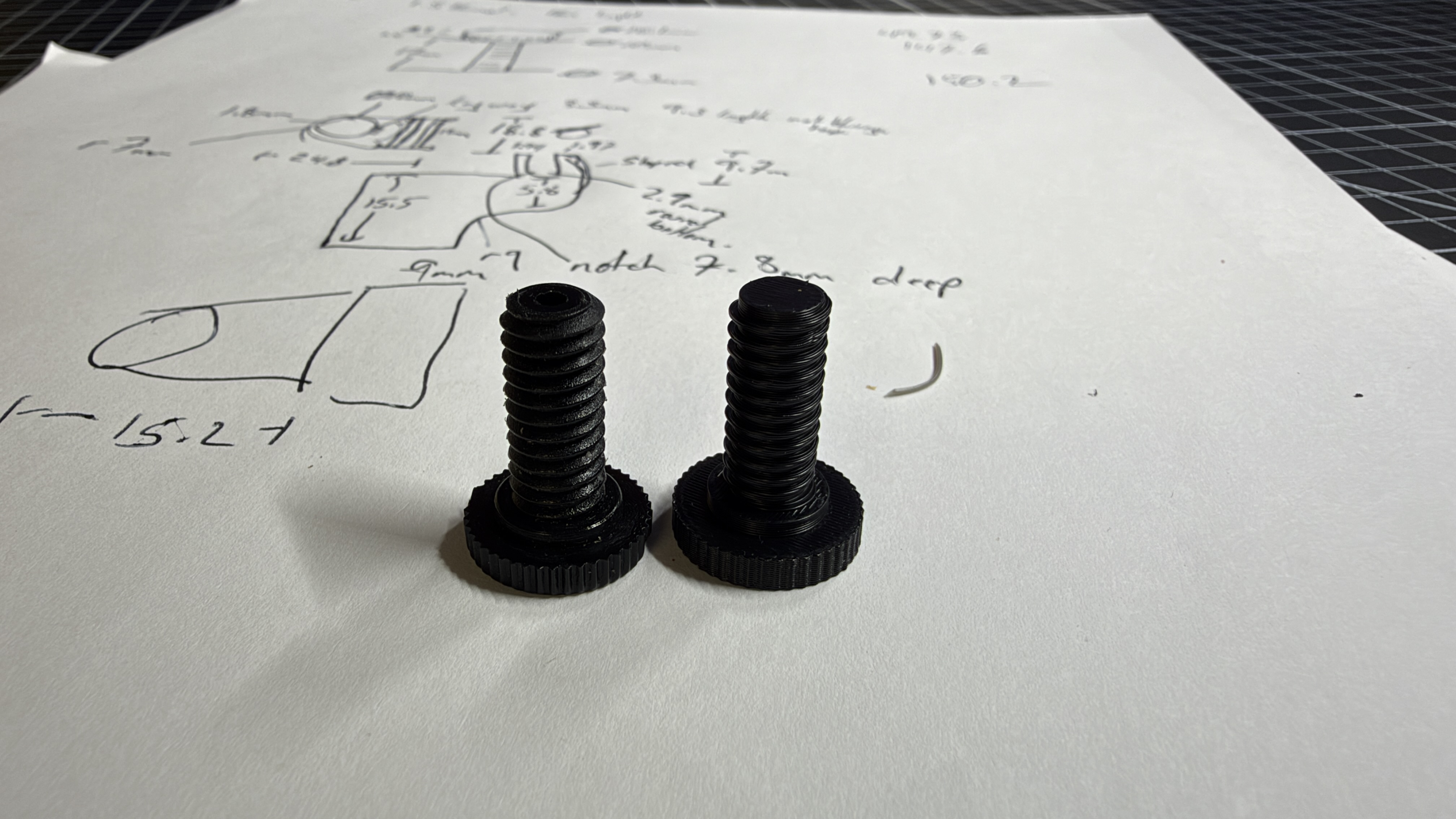 Two printed custom screw prototypes in front of hand-drawn measurements